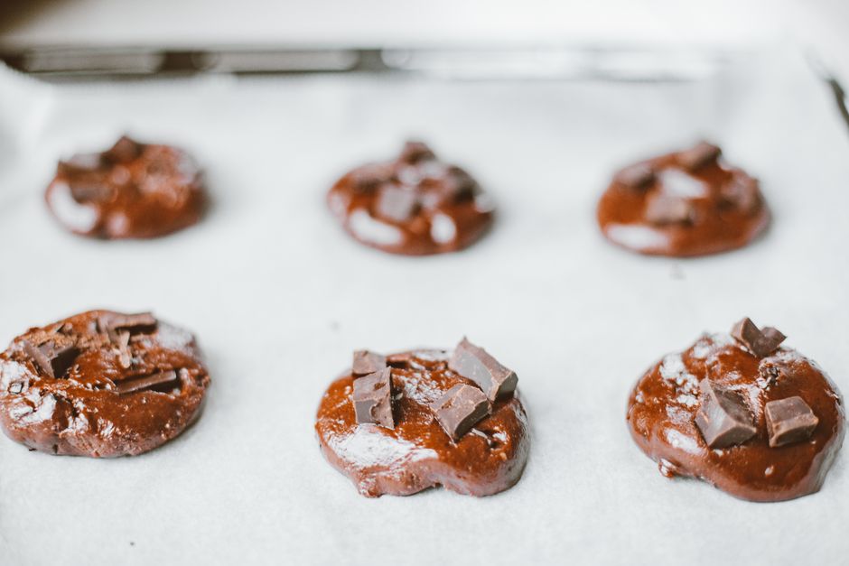 Close-up of chocolate cookie dough with chunks on a baking sheet.